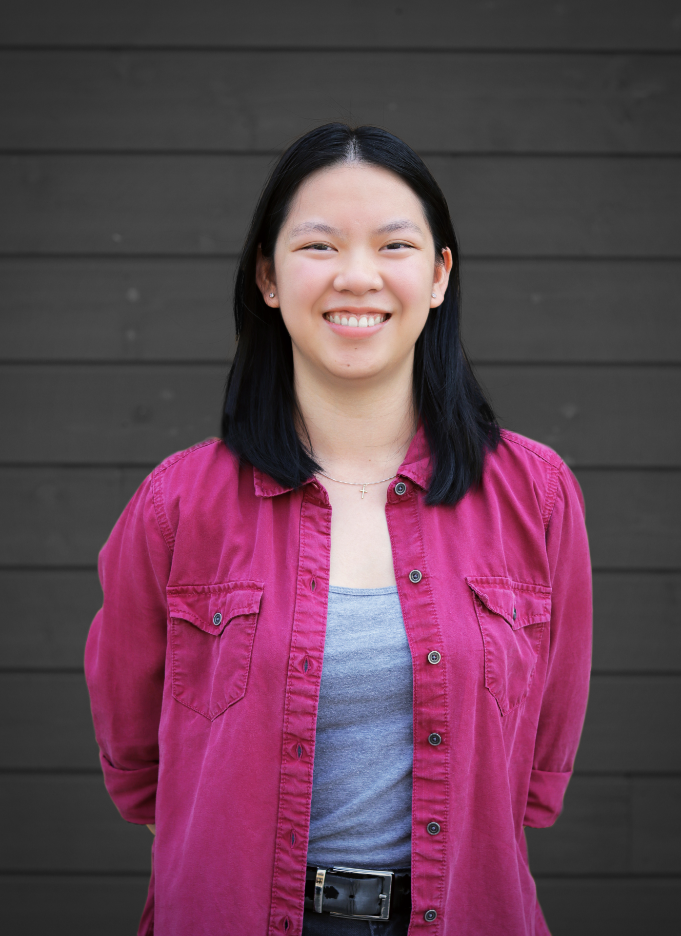 Asian woman in pink shirt and grey undershirt standing in front of wall with grey siding