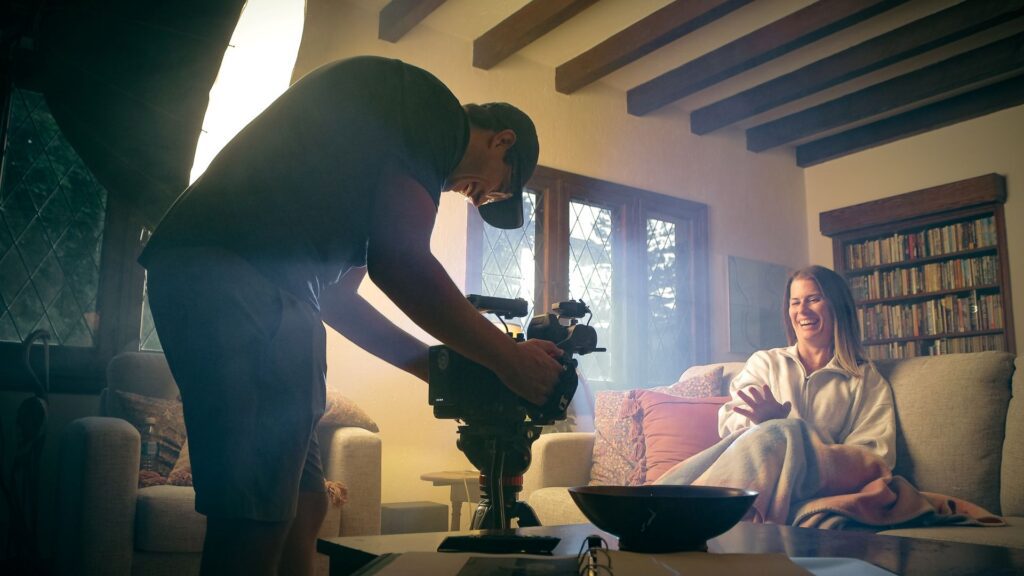 Videographer adjusts DJI Ronin 4D while laughing with a woman in a white sweater sitting on a grey couch